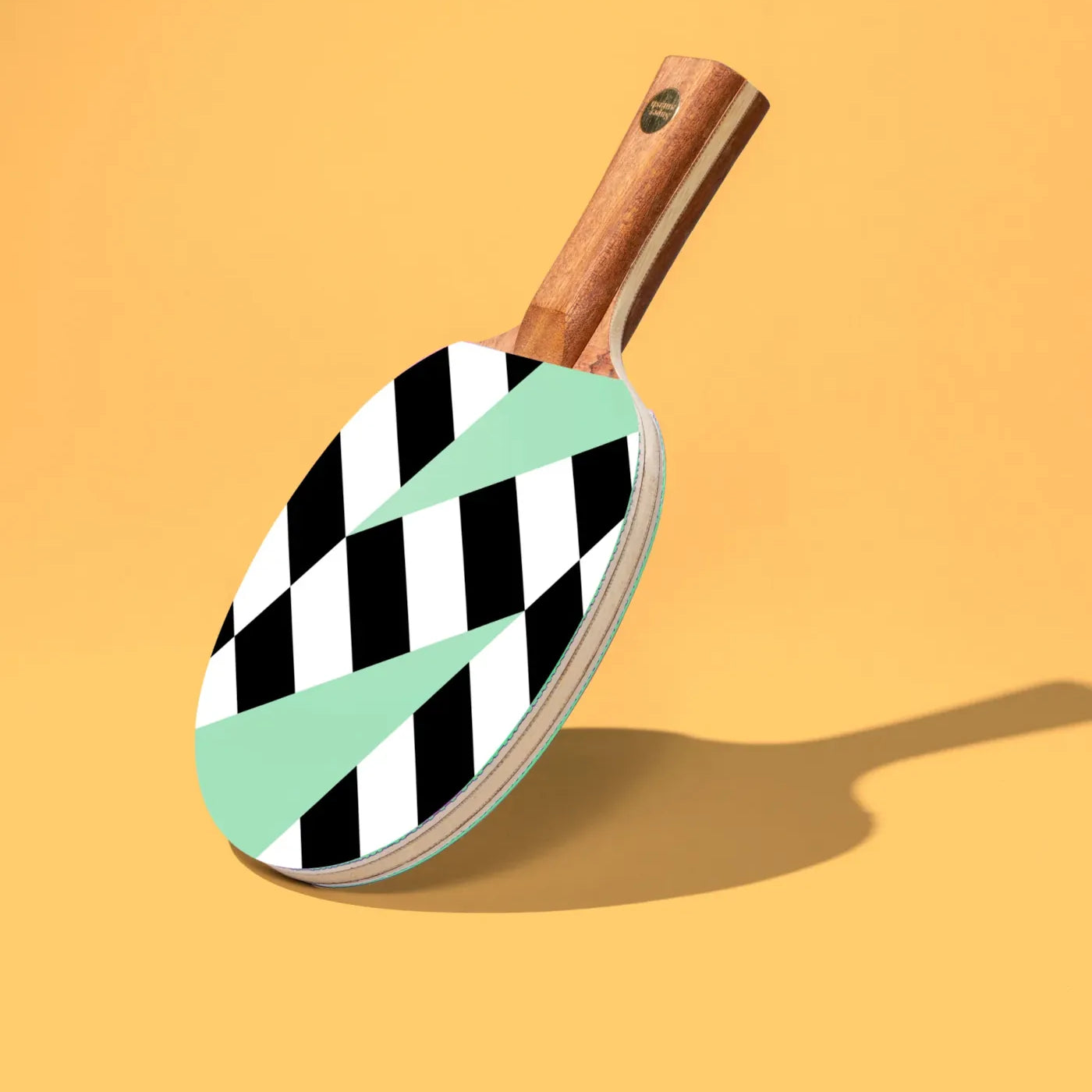 Pingpongschläger von Supersmash mit geometrischem Muster in Mint, Weiss und Schwarz auf gelbem Hintergrund.
