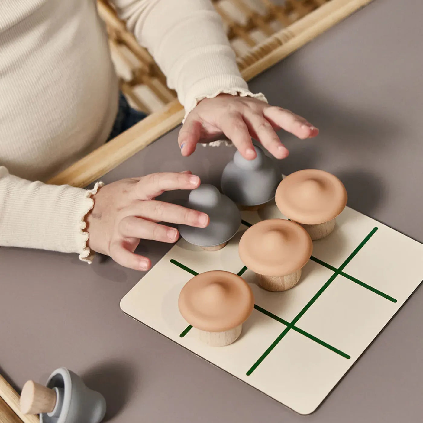 Kind spielt mit dem Tic-Tac-Toe-Spiel aus Holz von OYOY Living Design – mit runden Spielfiguren in Grau und Beige auf beiger Spielmatte.